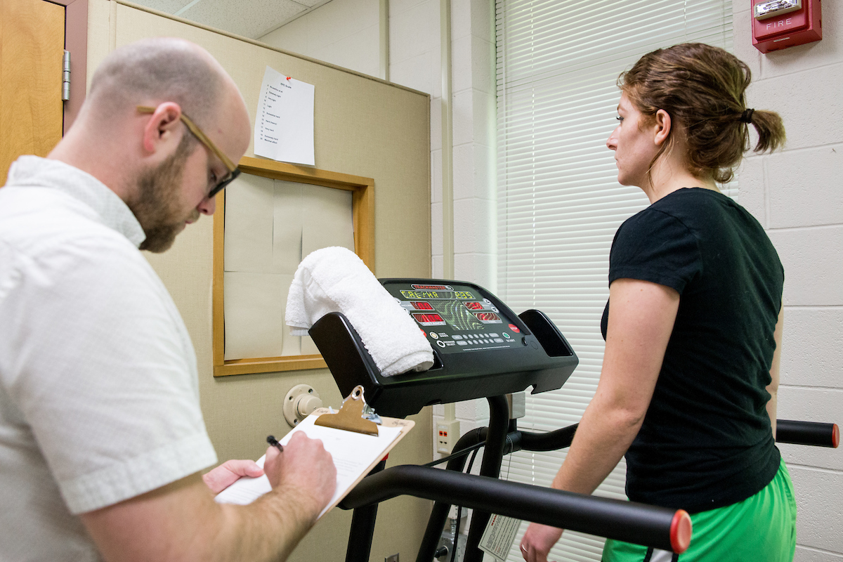 Student recording notes while another student walks on treadmill