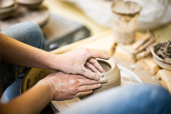 ceramics student refines the lip of a wheel-thrown container in the ceramics workshop