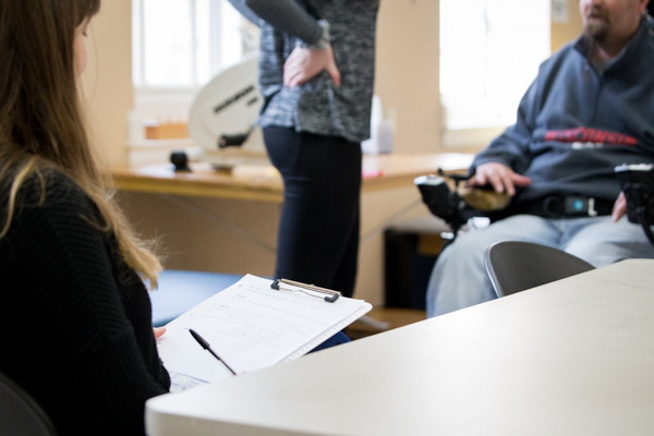 A person in wheelchair in the background and a person in foreground taking notes
